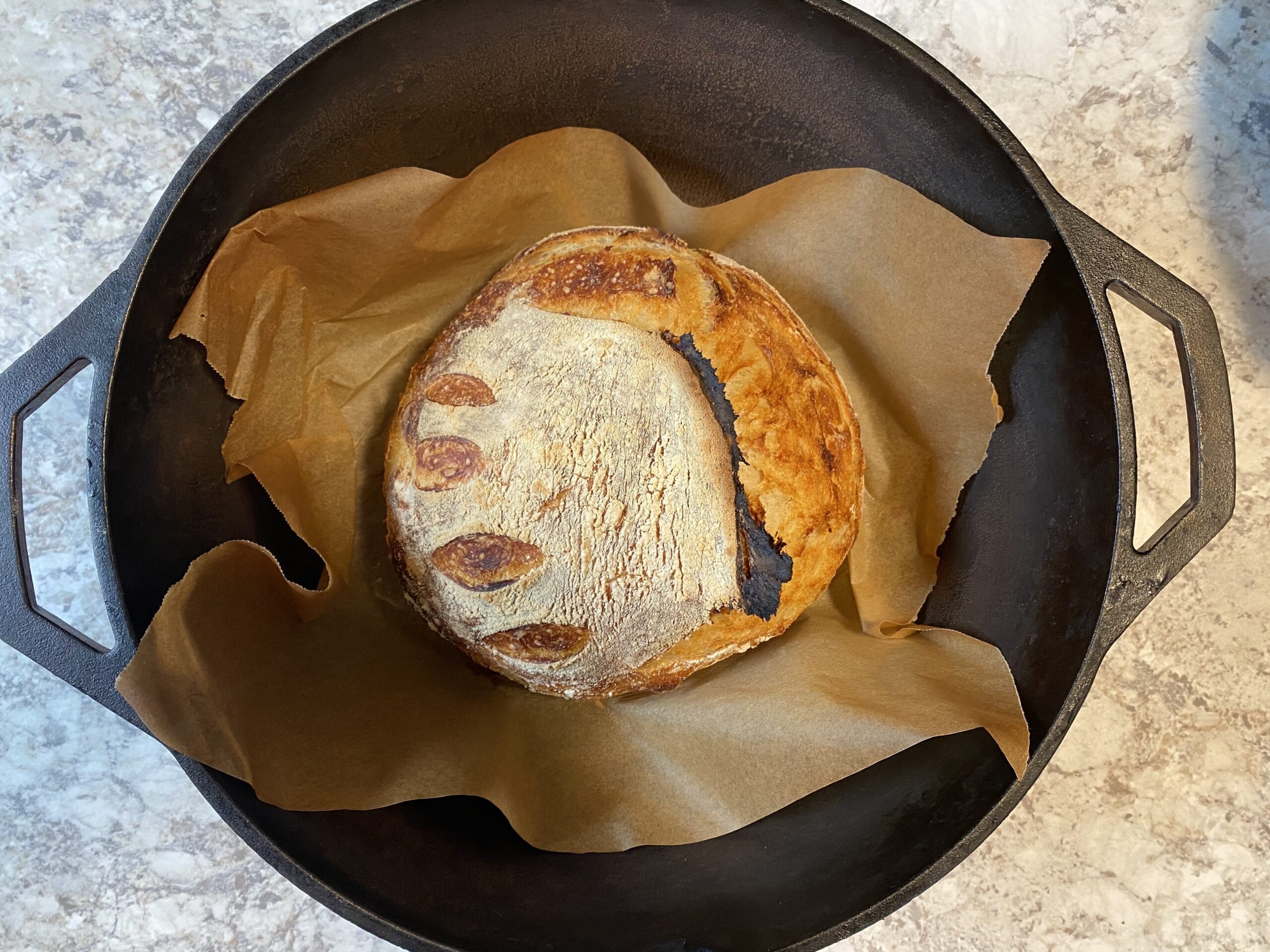 loaf of sourdough bread on parchment paper in Dutch oven