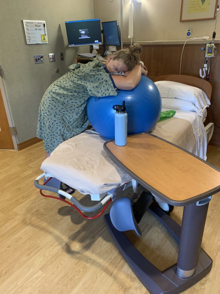 first time mom in labor leaning on birthing ball in hospital room