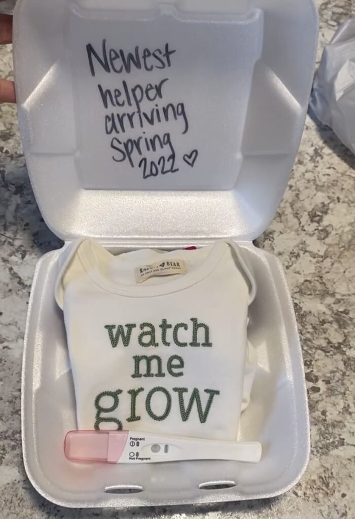 pregnancy announcement with positive test and baby onesie in to-go container